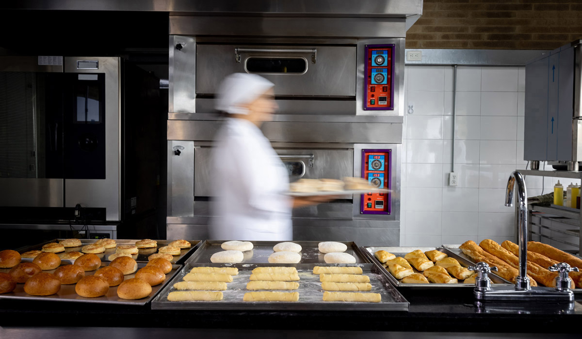 Woman walking past oven in bakery kitchen with baked goods on trays