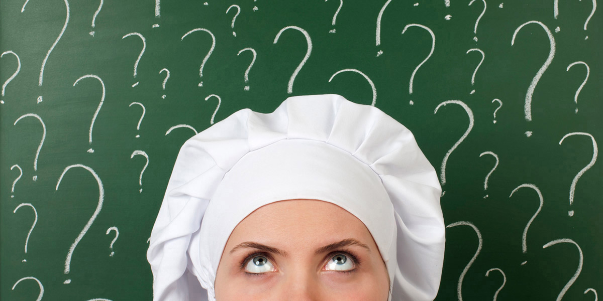 Woman with white baker hat looking up with question marks on a chalk board behind her