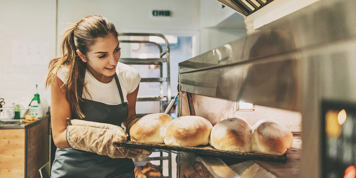 Female baker removing bread from the oven