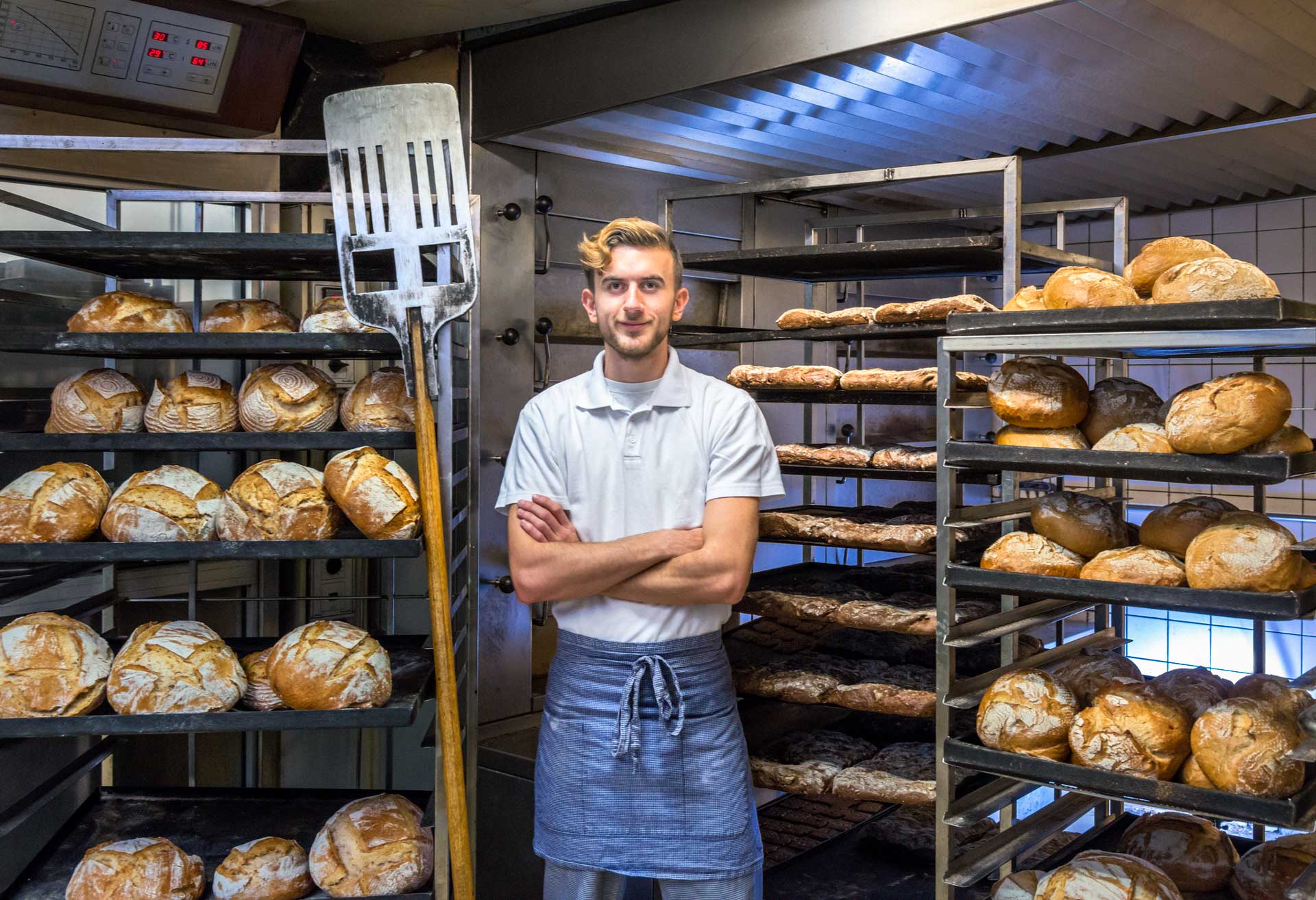 Male baker standign beside his bakery racks of bread