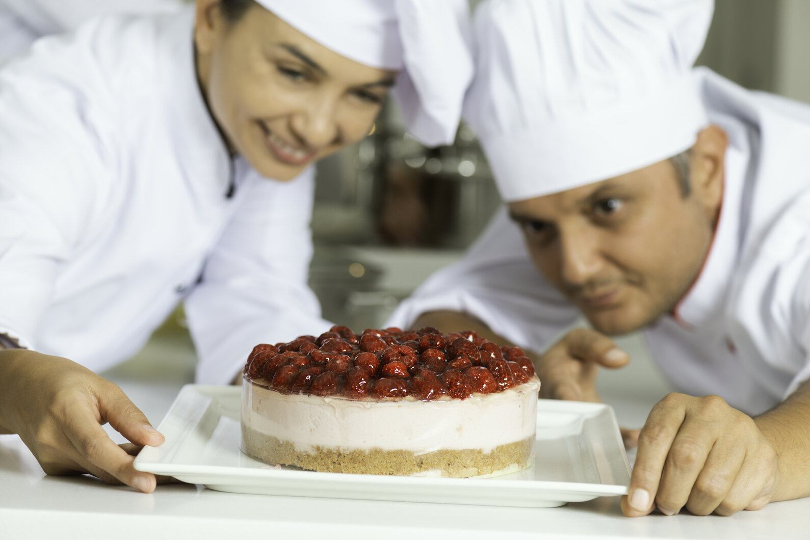 One female chef and one male chef are looking at cheesecake with raspberry in commercial kitchen.